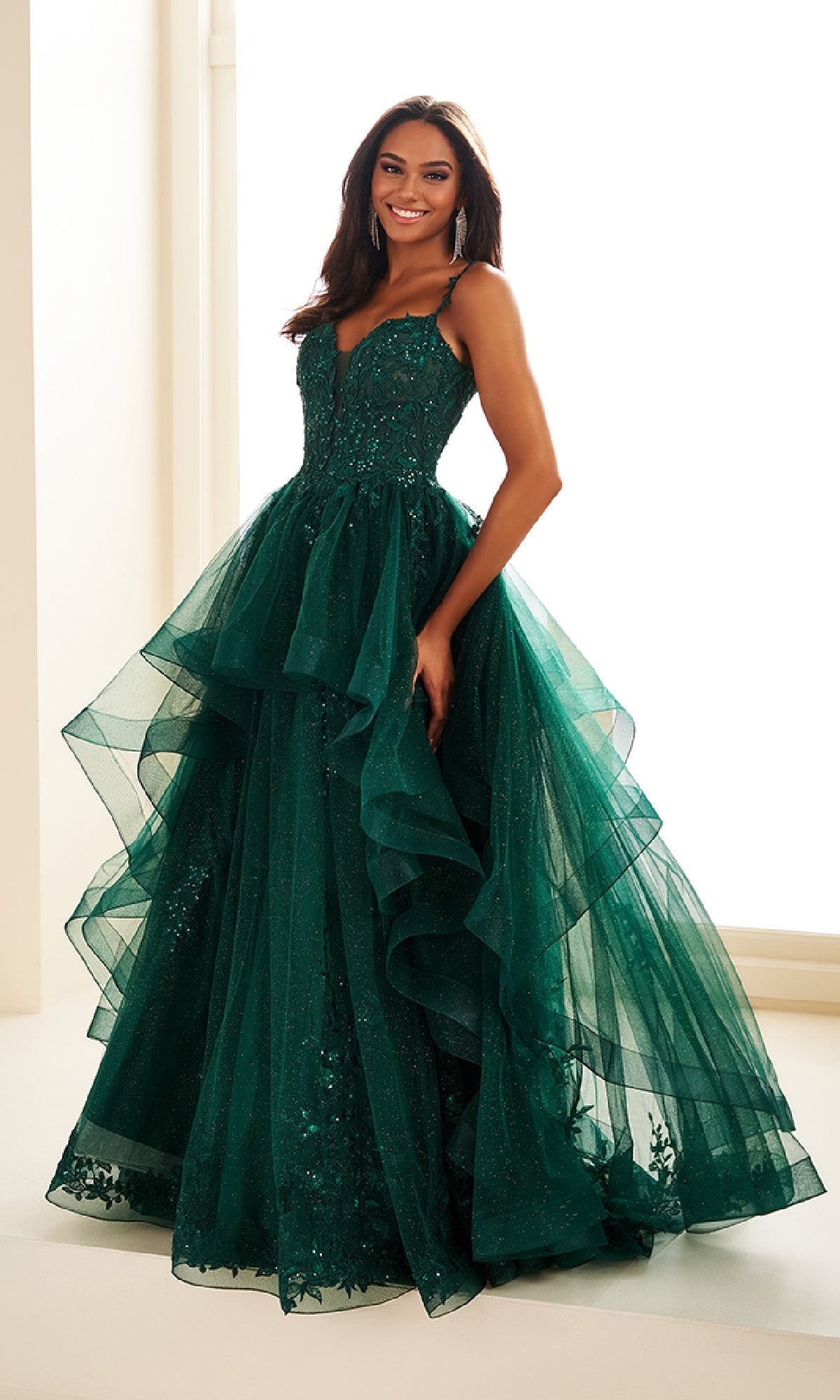 A woman smiles in the Ellie Wilde EW36081 long prom dress, featuring a fitted bodice, thin straps, and a voluminous green glitter tulle skirt adorned with sparkling details.